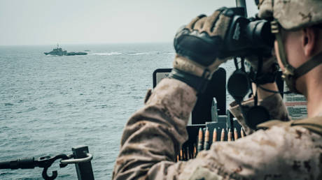 A U.S. Marine observes an Iranian fast attack craft from USS John P. Murtha during a Strait of Hormuz transit
