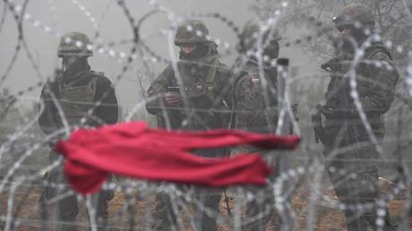 Polish servicemen stand guard behind a barbed wire as clothes are dried at a migrant camp on the Belarusian-Polish border in Grodno region, Belarus. © Sputnik / Viktor Tolochko
