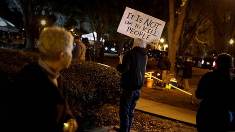 A man holds a sign that reads 'It is not ok to kill people' during a vigil for Ahmaud Arbery outside the Glynn County Courthouse. © REUTERS / Marco Bello