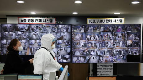 یک امدادگر از کنار صفحه نمایشی می گذرد و بیماران مبتلا به کووید را در بخش مراقبت های ویژه در کره جنوبی تماشا می کند.  © رویترز / کیم هونگ جی