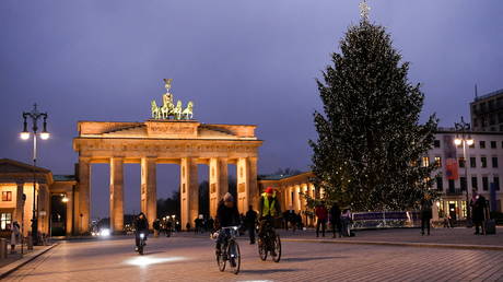 People pass a Christmas tree close to the Brandenburg gate in Berlin, Germany on December 21, 2021.