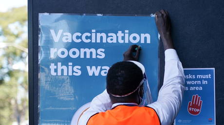 FILE PHOTO: A 'social distance marshall' straightens a sign outside a Covid-19 vaccination clinic in Sydney, Australia