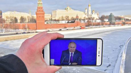 A person watches broadcast showing the annual end-of-year news conference of Russian President Vladimir Putin on a smartphone at the Bolshoi Kamenny Bridge, with the Moscow Kremlin in the background, Russia. © Sputnik / Alexey Kudenko