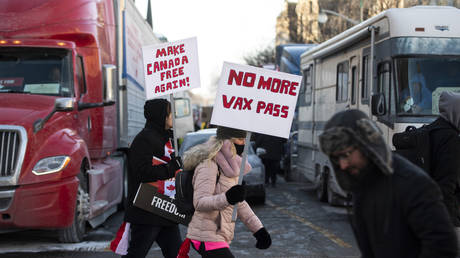 People walk in front of trucks parked on Wellington Street as they join a rally against COVID-19 restrictions on Parliament Hill, which began as a cross-country convoy protesting a federal vaccine mandate for truckers, in Ottawa, on Saturday, Jan. 29, 2022. © Justin Tang / The Canadian Press via AP