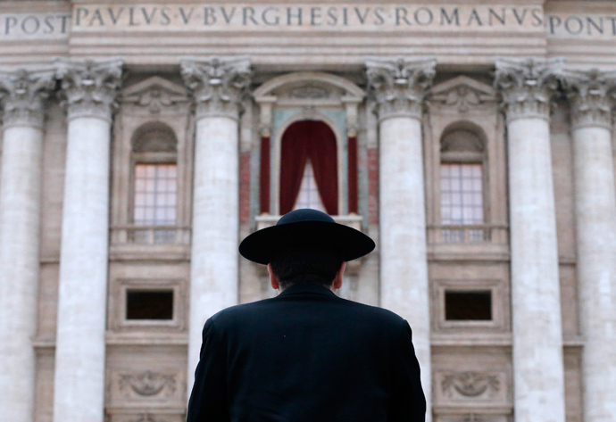 A priest stands in front of Saint Peter's Basilica as a red curtain has been put on the central balcony, called the Loggia of the Blessings, at the Vatican March 11, 2013 (Reuters / Christian Hartmann)