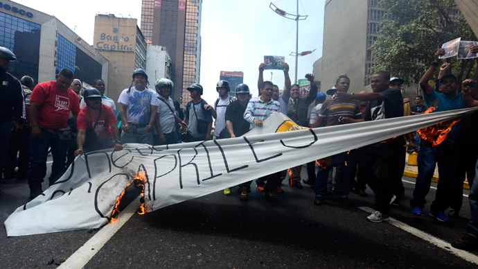Supporters of late President Hugo Chavez burn a banner of opposition presidential candidate Henrique Capriles in downtown Caracas on March 21, 2013 during a demonstration of opposition students demanding to the National Electoral Council (CNE) transparency during the presidential elections next February 14 (AFP Photo / Juan Barreto)