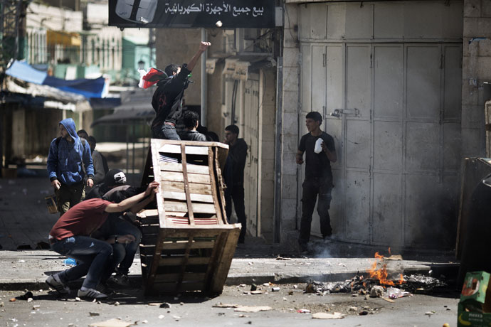 Palestinian demonstrators take cover behind a makeshift barricade during clashes with Israeli troops in the West Bank city of Hebron following the death of a Palestinian prisoner on April 2, 2013.(AFP Photo / Marco Longari)
