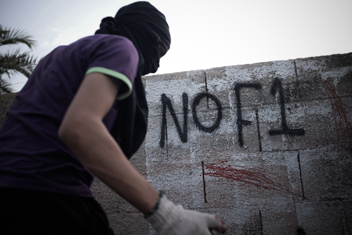 A Bahraini masked protestor writes graffiti against the upcoming Bahrain Formula One Grand Prix on the sidelines of an anti-regime rally in support of political activists held in jail in the village of Jid Ali, north-east of Isa Town, on April 17, 2013 (AFP Photo / Mohammed Al-Shaikh)