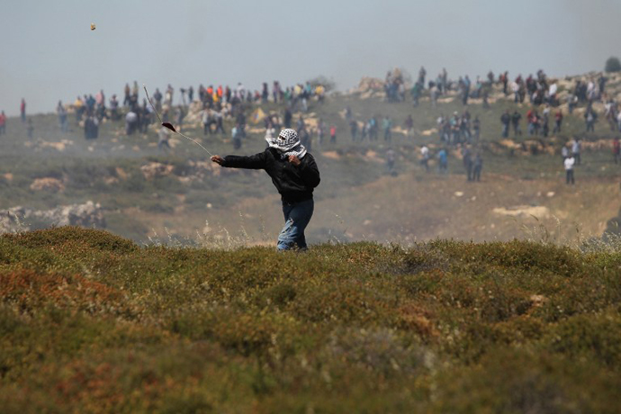 A Palestinian demonstrator uses a sling shot to throw rocks towards Israeli security forces during clashes following a march against construction on their land by members of the Jewish settlement of Ofra on April 26, 2013. (AFP Photo / Abbas Momani)