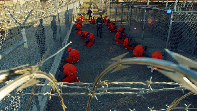 Detainees in orange jumpsuits sit in a holding area under the watchful eyes of military police during in-processing to the temporary detention facility at Camp X-Ray of Naval Base Guantanamo Bay.(Reuters / Stringer)