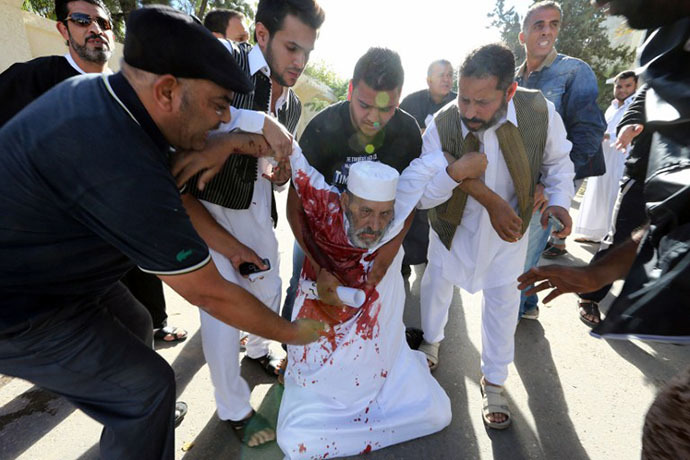 People assist a man who was injured after Libyan militiamen opened fire on a crowd wanting them to move out of their headquarters on November 15, 2013 in southern Tripoli. (AFP Photo / Mahmud Turkia)