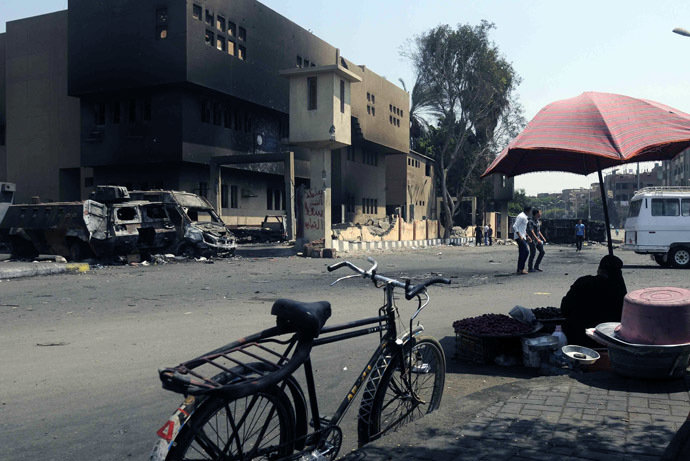 An Egyptian street vendor sits opposite a torched and vandalized police station on August 24, 2013 in the Kirdasah neighbourhood of Giza, on the outskirts of Cairo, that was attacked on August 14, resulting in the death of at least seven policemen following a crackdown by Egyptian security forces on protest camps and sit-ins held by supporters of the Muslim Brotherhood and ousted president Mohamed Morsi.(AFP Photo)