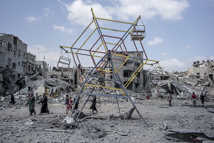 Palestininans go their way past rubbles and a mini ferris wheel in the northern district of Beit Hanun in the Gaza Strip, during an humanitarian truce, on July 26, 2014. (AFP Photo / Marco Longari)