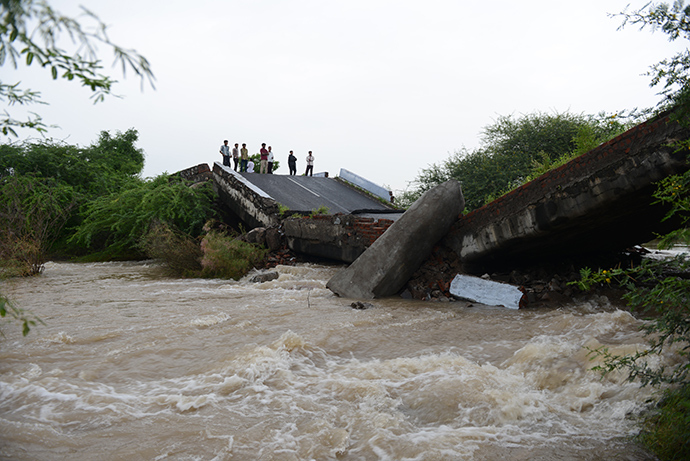 Indian villagers watch flood waters flow beneath a collapsed bridge due to heavy rains at Tagdi village on Dhaduka - Bhavnagar Highway, some 110 kms from Ahmedabad on September 9, 2014 (AFP Photo / Sam Panthaky)