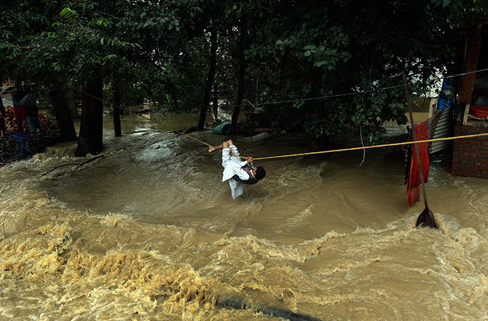 An Indian Kashmiri man crosses over flood waters with the use of a rope in Srinagar on September 9, 2014 (AFP Photo / Punit Paranjpe)