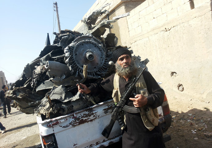 An armed jihadist stands next to the wreckage of a Syrian government forces aircraft which was shot down by militants of the Islamic State (IS) group over the Syrian town of Raqa (AFP Photo / RMC / Str)