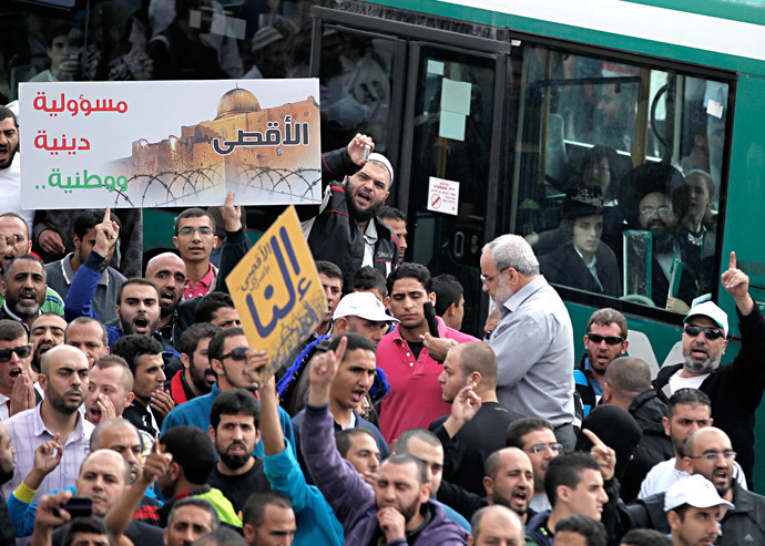 Palestinians shout slogans while Orthodox Jews look at the scene from a bus passing by, during a rally near the entrance of al-Aqsa mosque compound to protest after authorities restricted access to the esplanade on October 15, 2014 outside Jerusalem's Old City. (AFP Photo / Ahmad Gharabli)