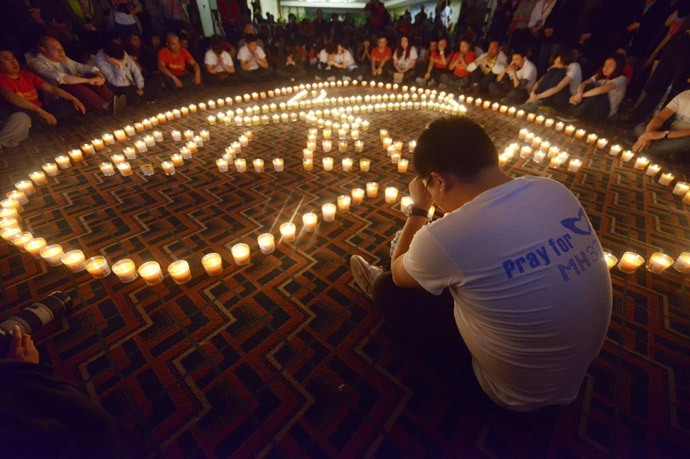 A Chinese relative (R) of passengers on Malaysia Airlines flight MH370 prays in front of candles as he takes part in a prayer service at the Metro Park Hotel in Beijing (AFP Photo / Wang Zhao)