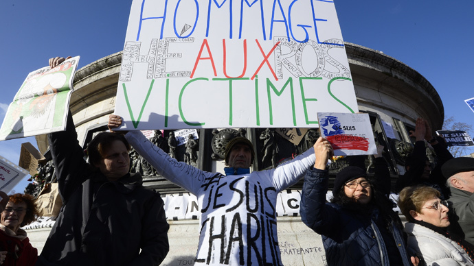 A man holds a cardboard reading "Hommage to the Victims-Heros" as people gather on the Place de la Republique (Republic Square) in Paris before the start of a Unity rally âMarche Republicaineâ on January 11, 2015 (AFP Photo / Bertrand Guay)