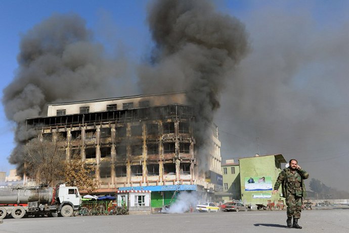 An Afghan National Army (ANA) soldier (R) talks on his mobile phone near a burning public market building in Pashtunistan square where clashes between Taliban-linked militants and security forces occured in Kabul on January 18, 2010. (AFP Photo / Massoud Hossaini)