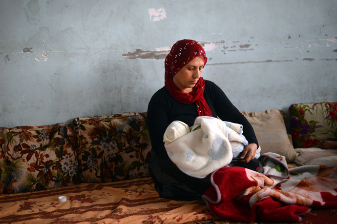 A Syrian Kurdish refugee from the majority-Kurdish Sheikh Maqsud district of the northern Syrian city of Aleppo, holds her baby in a school used as a refugee camp in the northern city of Afrin (AFP Photo / Dimitar Dilkoff)