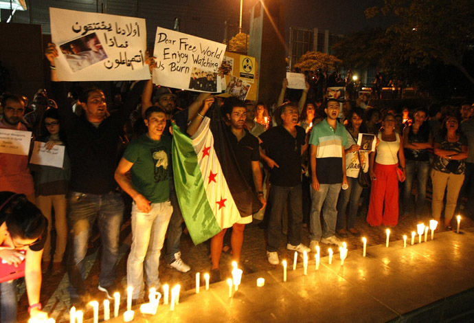 Lebanese and Syrian civilians hold signs and Syria's former independence flag which has been adopted by the rebels forces fighting against Syrian pro-government forces as they take part in a candle lit vigil in front of the offices of the United Nations headquarters in Beirut, in solidarity with Syrian civilians who were killed in attacks in the suburbs of Damascus on August 21, 2013. (AFP Photo)