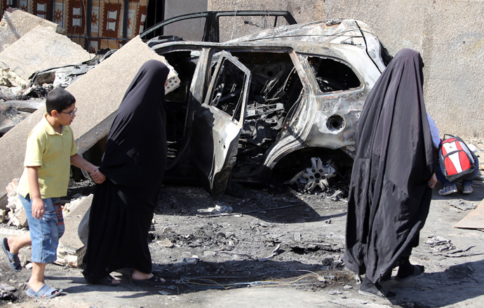 Iraqi women wlak past a burnt-out vehicle on October 7, 2013 following a bombing attack in Baghdad's eastern al-Jadidah district the night before. (AFP Photo / Ahmad Al-Rubaye)
