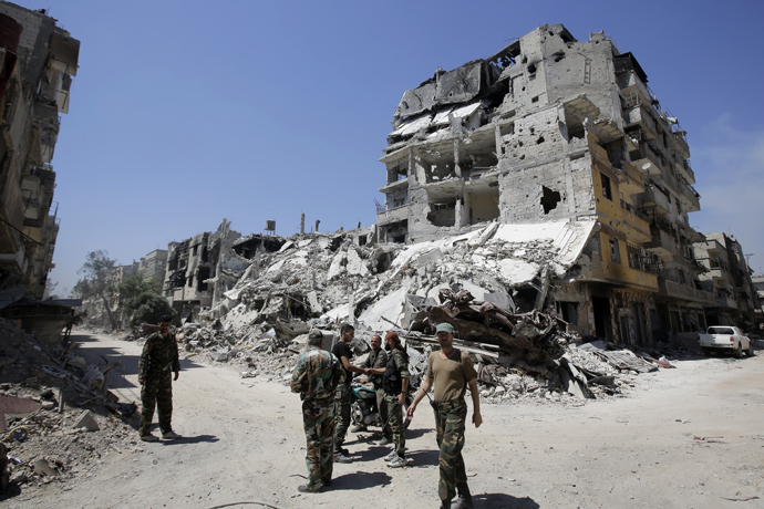 Soldiers of the Syrian government forces patrol on a tank in a devastated street (AFP Photo)