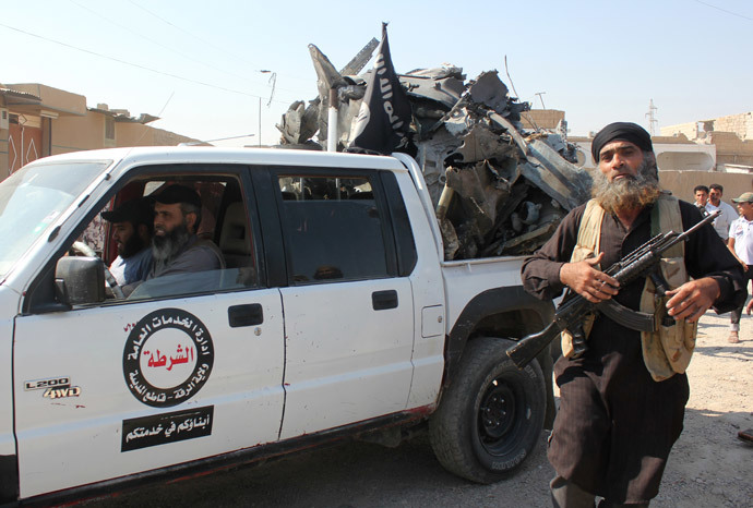 An Islamic gunman walks past a pick up truck belonging to the "Raqa Regional Public Service" headed by the Islamic State (IS) group loaded with the wreckage of a Syrian government forces aircraft which was shot down by IS' militants over the Syrian town of Raqa (AFP Photo / Str)