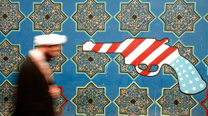 An Iranian cleric walks past a mural on the wall of the former U.S. embassy in Tehran 